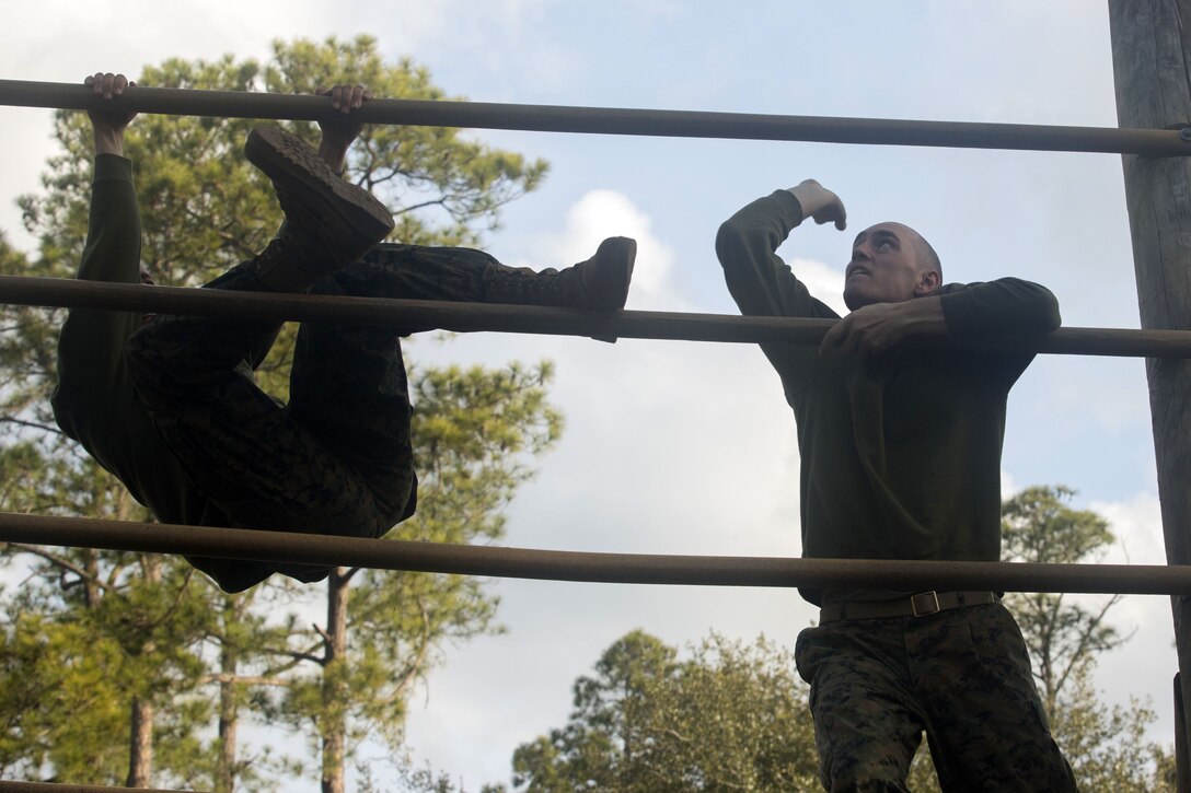 Two Marines climb bars.