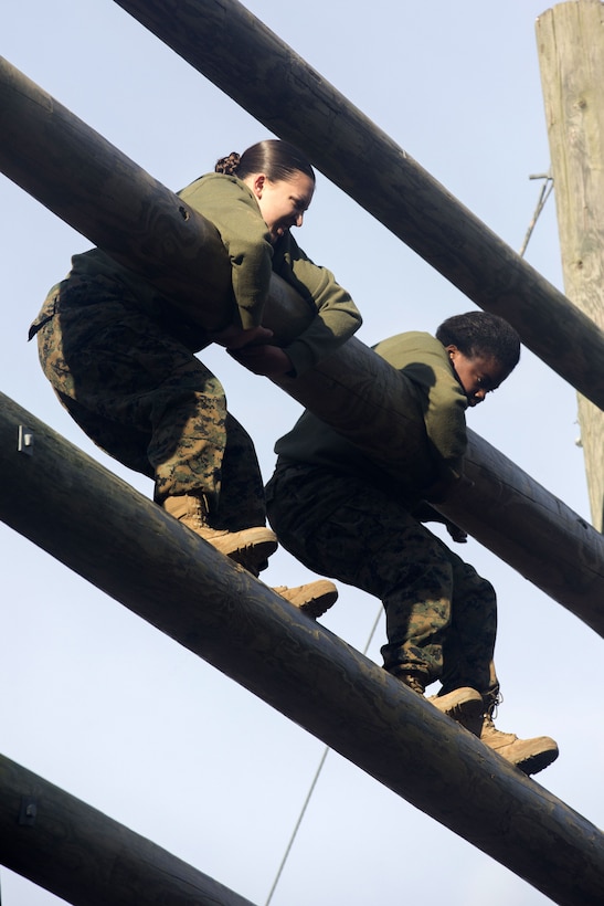 Two Marines climb up a tower with logs.