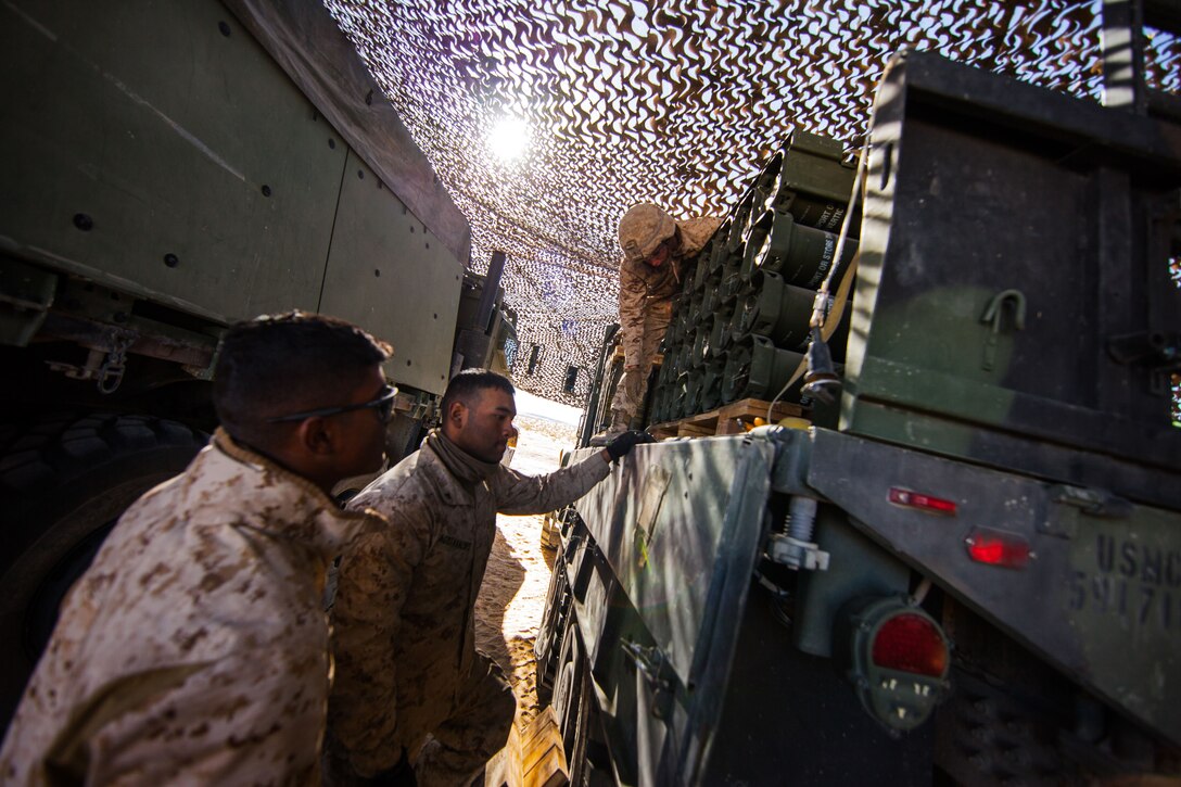 Marines stand near the back of a truck holding ammo cans.