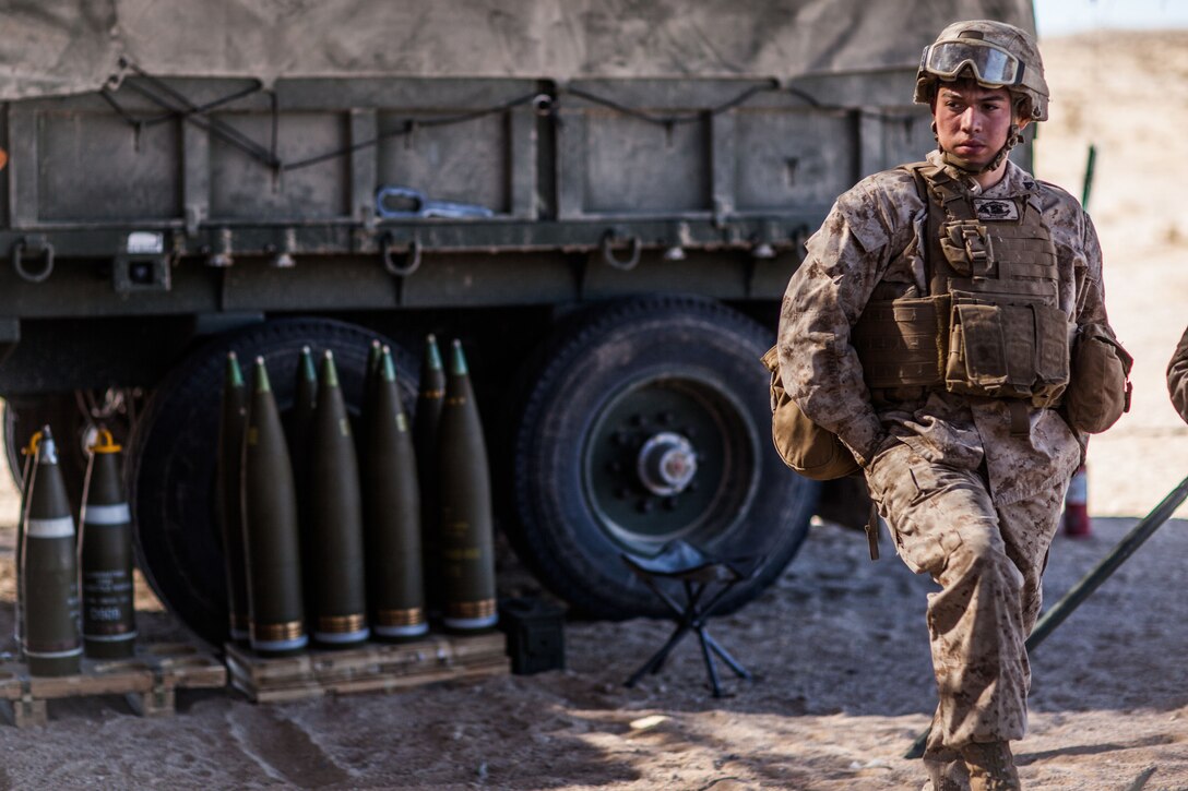 A Marine stands next to a military vehicle and ammo.