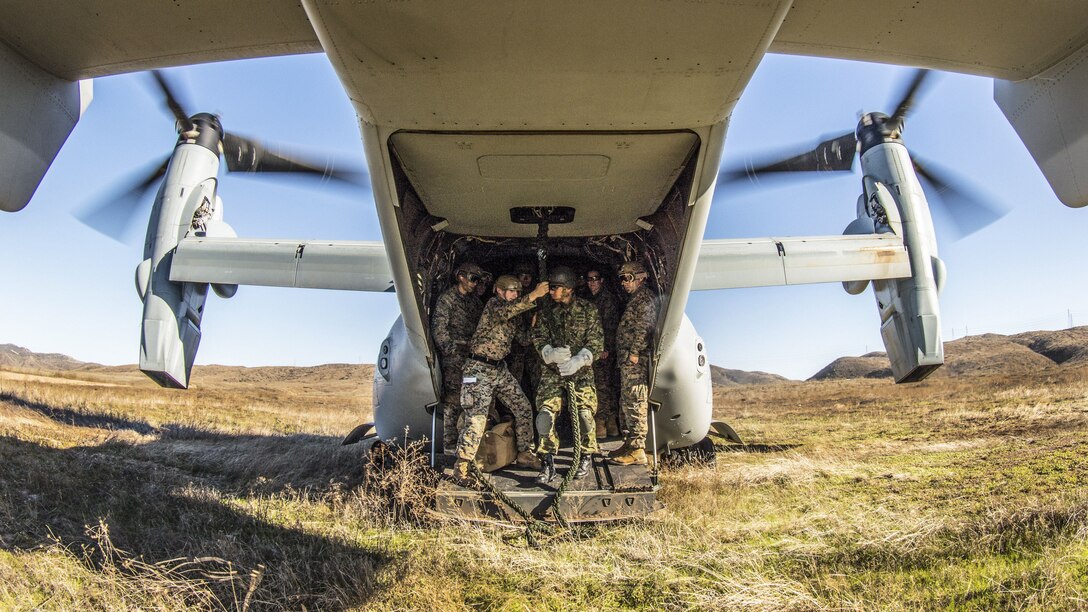 A group of Marines crowds around a rope in the back of an aircraft parked in a field.