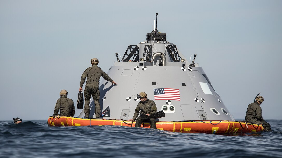 Sailors sit on a dummy space capsule floating in the sea.