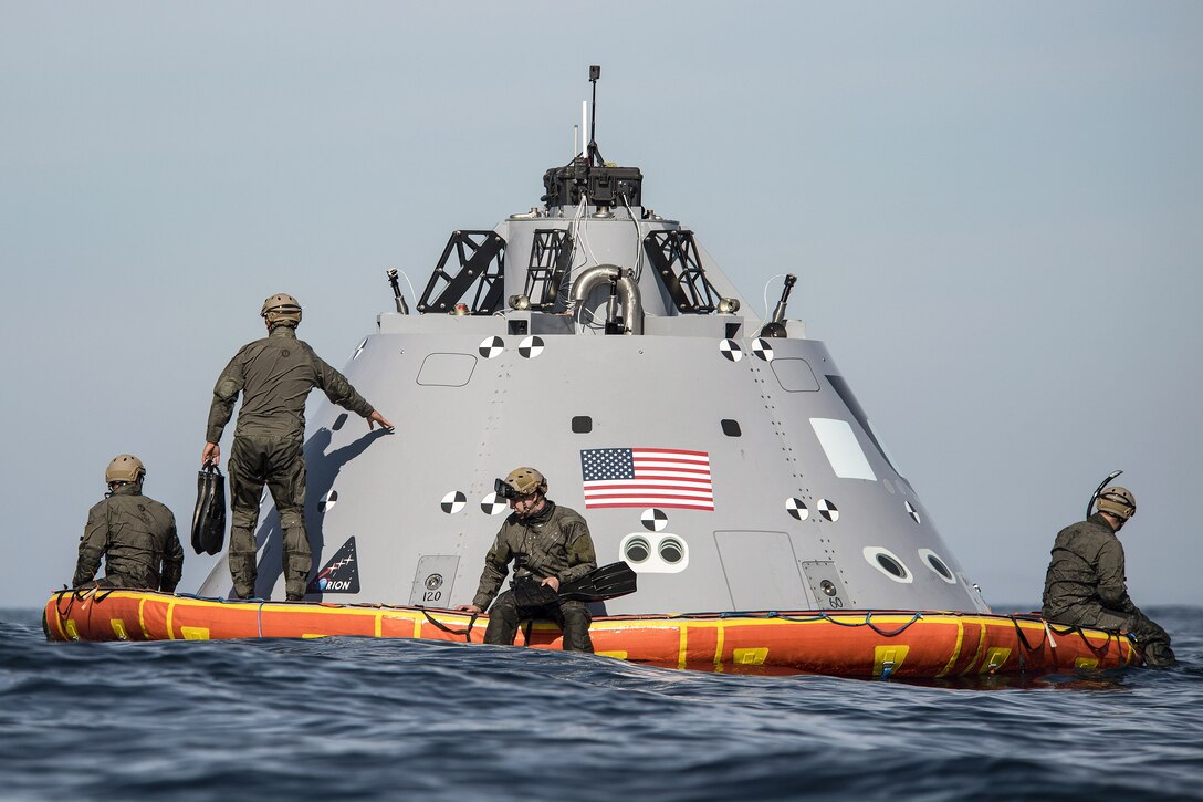 Sailors sit on a dummy space capsule floating in the sea.