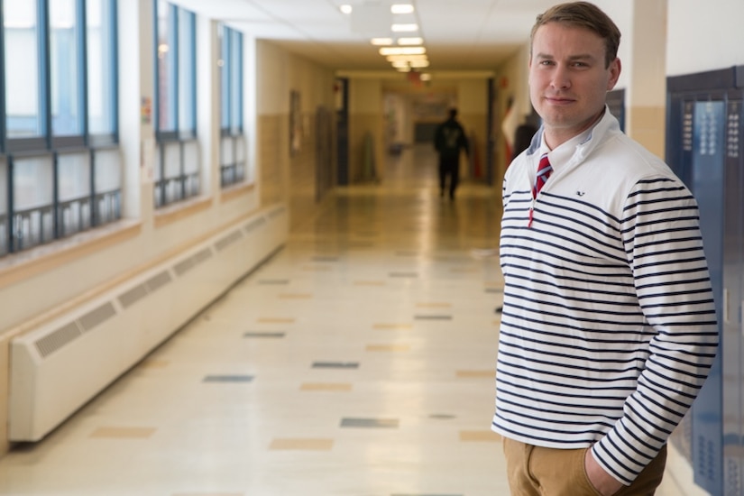 A teacher stands in the hallway of a school.