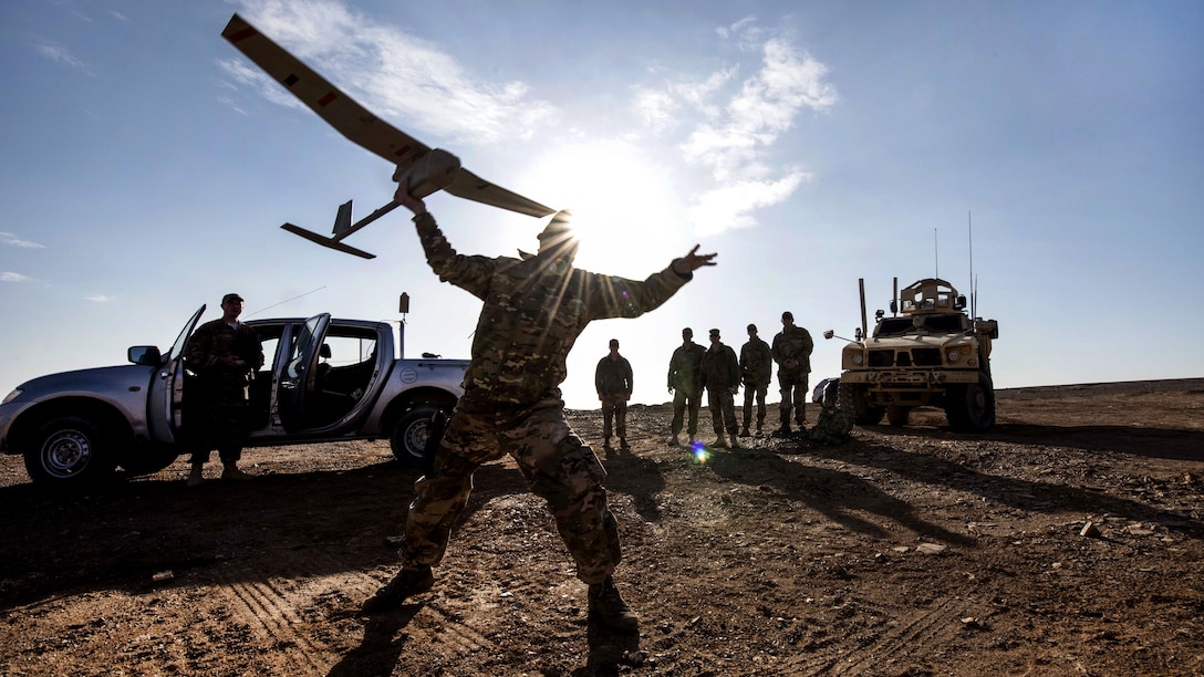 An silhouetted airman launches a drone in an open area.