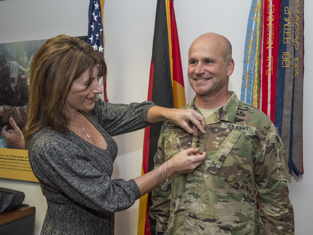 A woman puts her husband's new rank on his uniform.