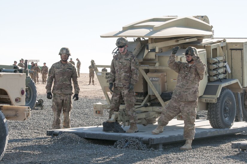 Spc. Aaron Harness, center, a motor transport operator, 1072nd Transportation Company, keeps track of a humvee’s progress as it reverses toward a pallet with a satellite transportable terminal during an emergency deployment readiness Jan. 12, 2018, at FOB Gerber on the Udairi Range Complex near Camp Buehring, Kuwait. The transportation unit moved the signal equipment from Camp Buehring to the FOB as the 115th Signal Battalion practiced rapidly emplacing and connecting signal equipment in support of emergency operations.