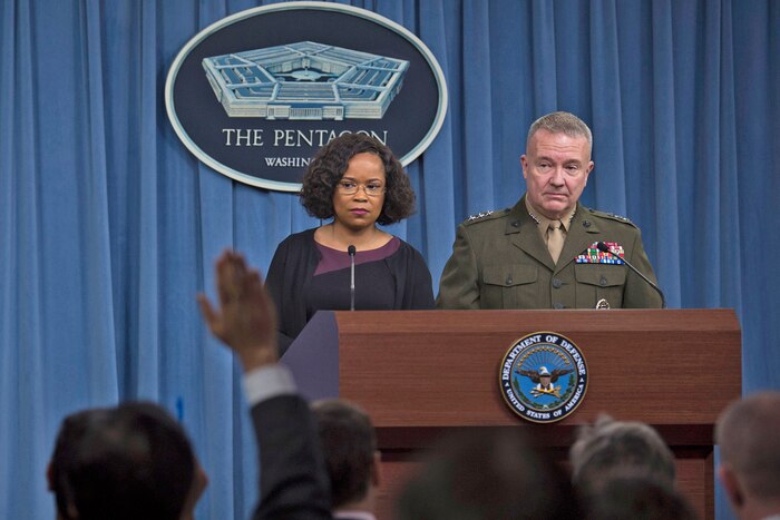 Two people stand behind a podium and answer questions during a news briefing.