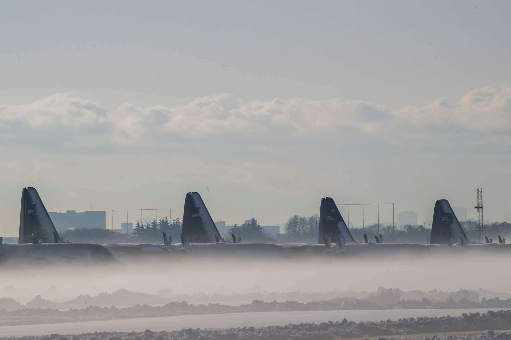 A row of C-130J Super Hercules sit on the flightline during a snow storm, Jan. 23, 2018, at Yokota Air Base, Japan.