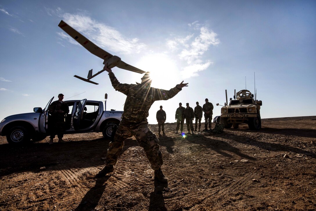 An silhouetted airman launches a drone in an open area.