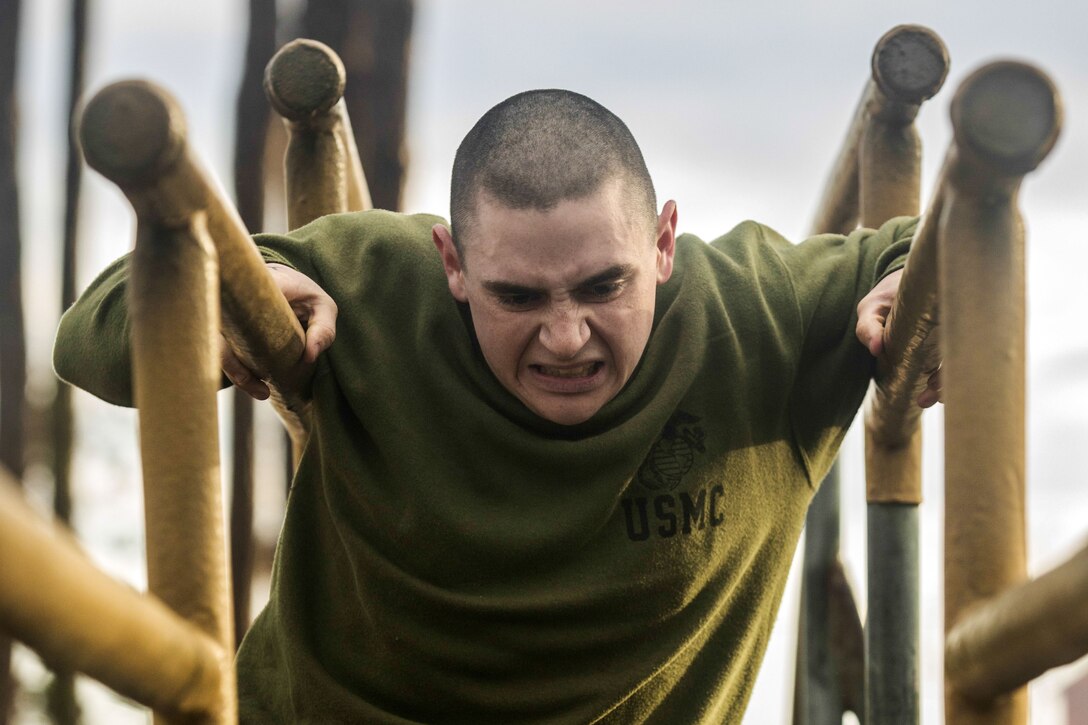 A Marine in an olive workout shirt scowls while holding himself up between two log poles