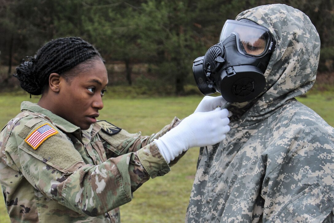 A soldier helps another soldier remove a chemical protective suit.
