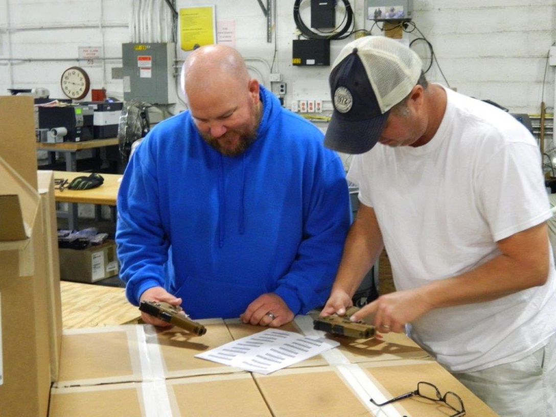 Douglas Wilson (pictured left) and Jarred Slaton, DDAA warehouse packers, verify the correct stock numbers with the weapons prior to packing.