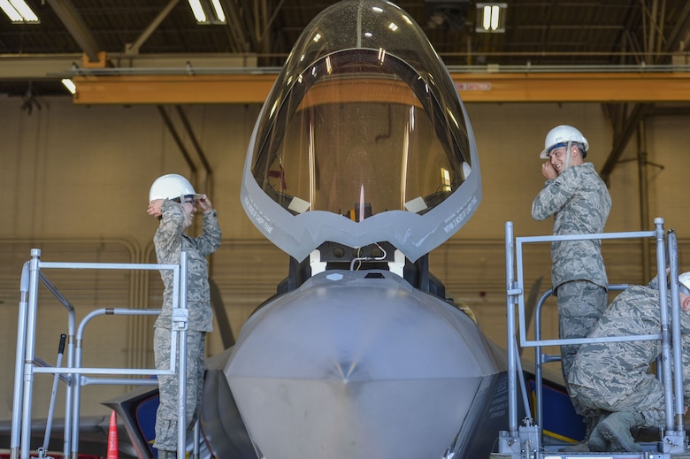 Airman 1st Class Raena Sadowski and Airman 1st Class Matthew Romano, 56th Component Maintenance Squadron egress systems technicians, put on safety helmets before the removal of an ejection seat from an F-35A Lightning II at Luke Air Force Base, Ariz., Jan. 11, 2018. In May 2017, three modifications were implemented to the F-35 ejection system to remove the 136 pound weight limit restriction. (U.S. Air Force photo/Airman 1st Class Caleb Worpel)
