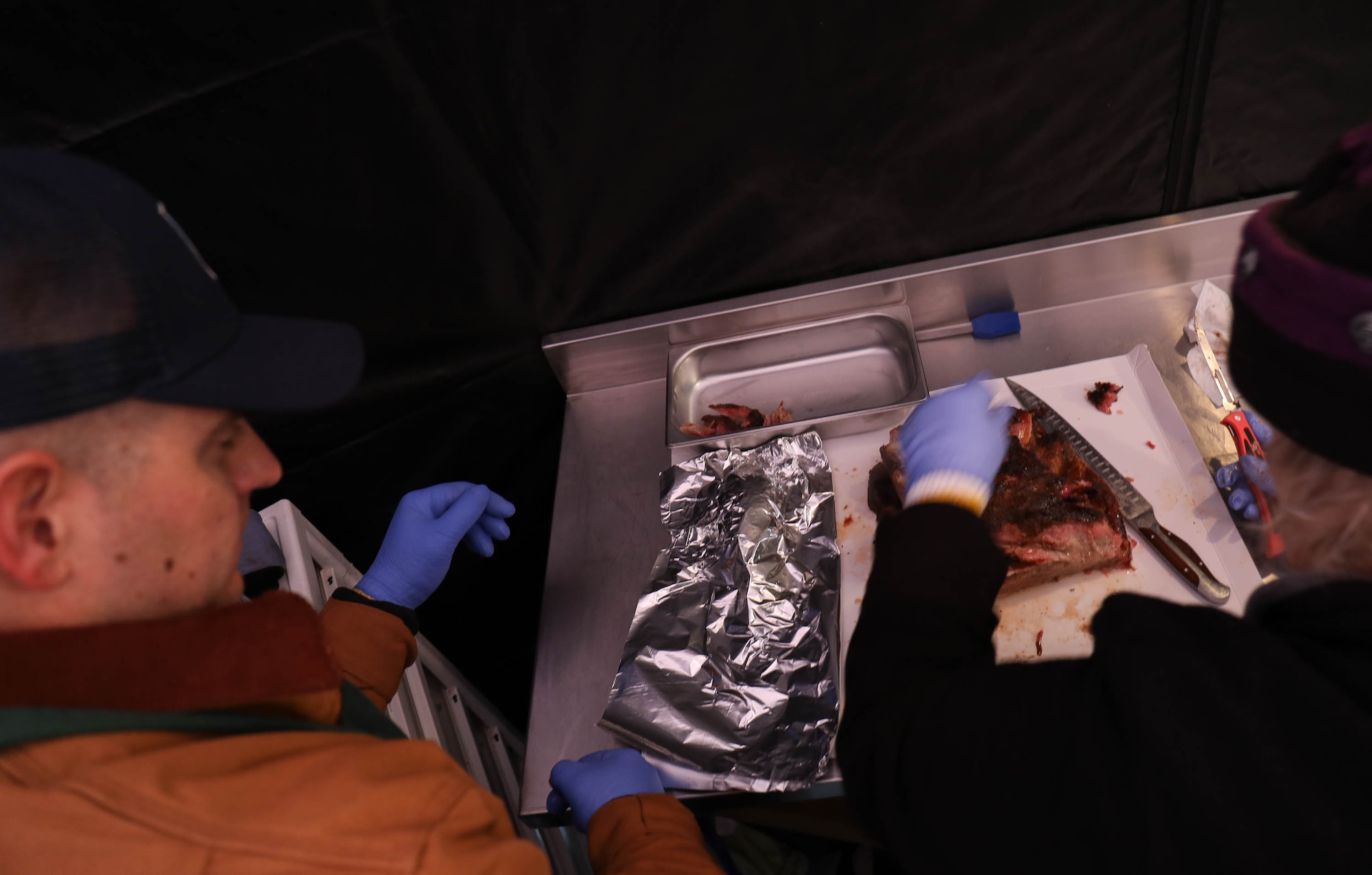 Tech. Sgt. John Hillenbrand of the 446th Airlift Wing watches as his barbecue mentor, Dianne Mee, slices a pork butt Jan. 19, 2018, on Joint Base Lewis-McChord. Barbecue prepared by Washington State pitmasters, paired with members of both the 62nd and 446th Airlift Wings, was served to JBLM personnel free of charge.