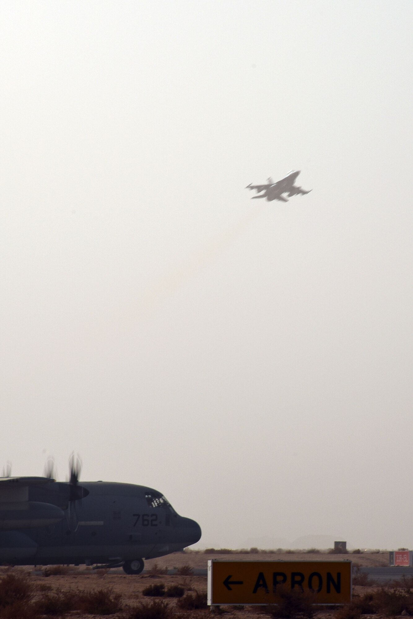 A C-130 Hercules waits to taxi while an F-16 Fighting Falcon takes off at an undisclosed in Southwest Asia, Jan. 20, 2018. The F-16 and pilot belong to the 100th Expeditionary Fighter Squadron, which flew approximately 850 sorties during their deployment. (U.S. Air Force photo by Staff Sgt. Joshua Edwards/Released)