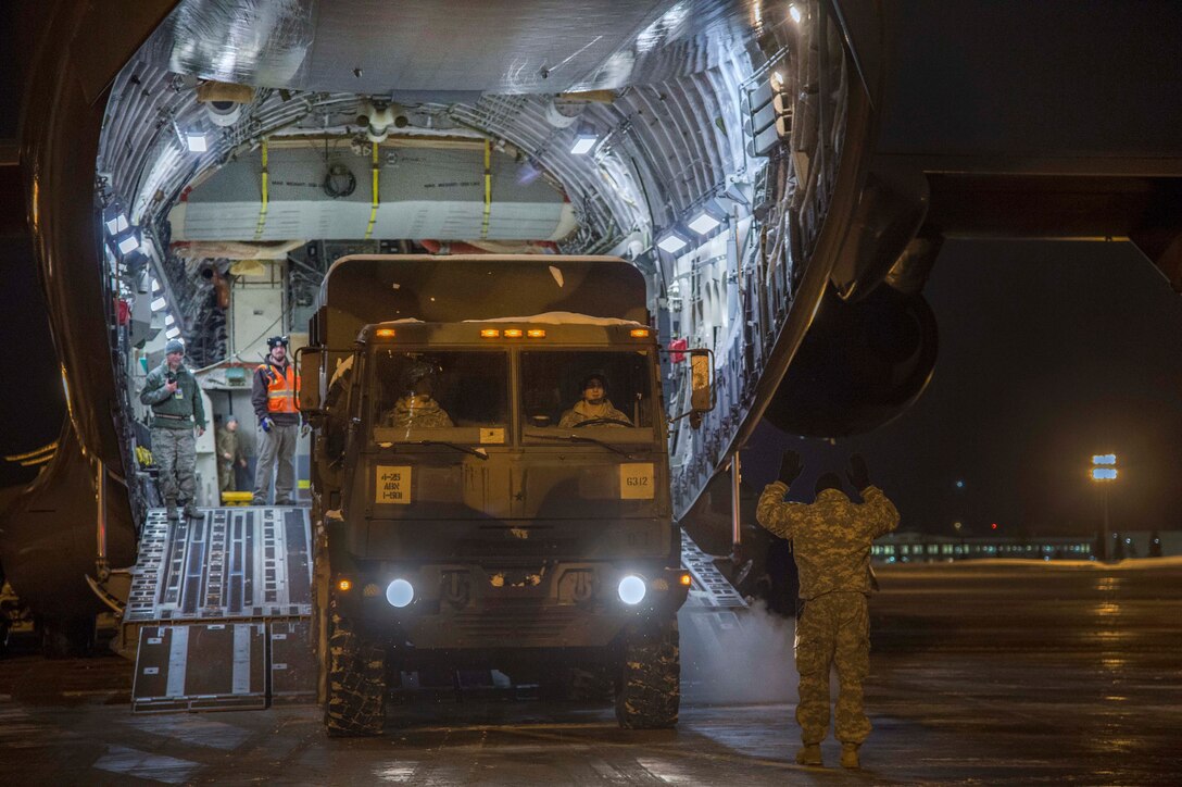A soldier directs a driver loading a vehicle onto a military aircraft.