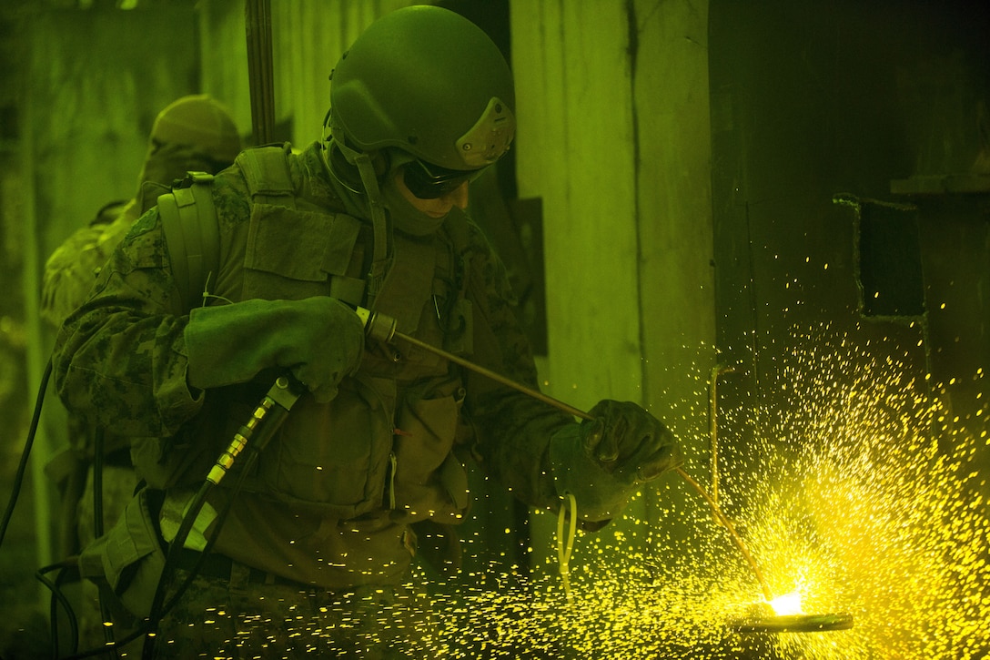 A Marine from Methods of Entry School on Marine Corps Base Quantico uses a torch to cut a through a ship door. This photo was taken with shade 5 safety goggles over the camera lens. Marines assigned to MOES come from different MOS's such as Reconnaissance and Force Reconnaissance units, Security Forces Regiment Recapture Tactics teams, Military Police Special Reaction teams, Explosive Ordnance Disposal units and Marine Special Operations Command units.