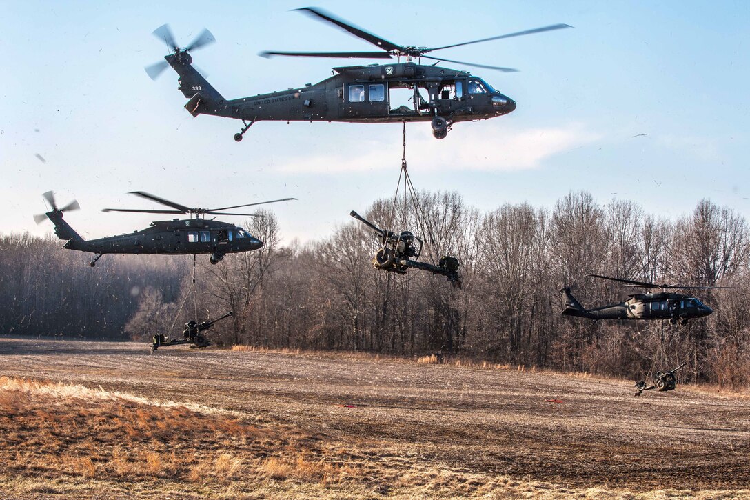 Three UH-60 Black Hawk helicopters slingload M119A3 howitzers to transported to a firing range during air assault operation at Fort Campbell, Kentucky.