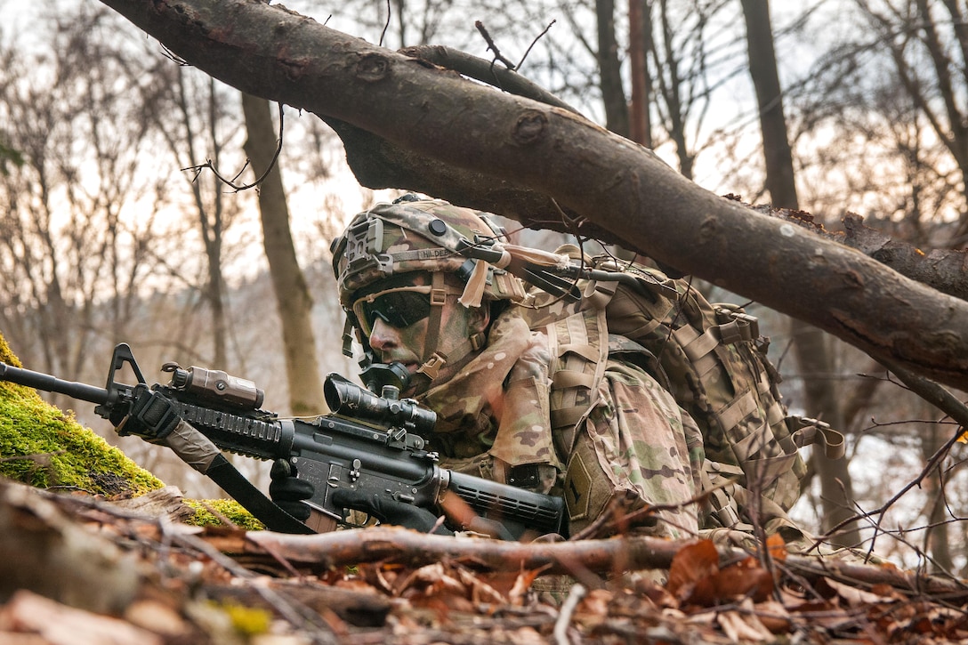 A soldier with a rifle laying in a wooded area.