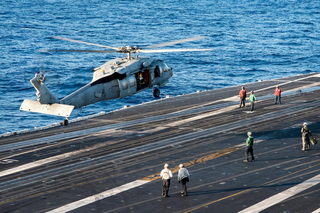 A military helicopter prepares to land on the flight deck of the aircraft carrier USS Carl Vinson.