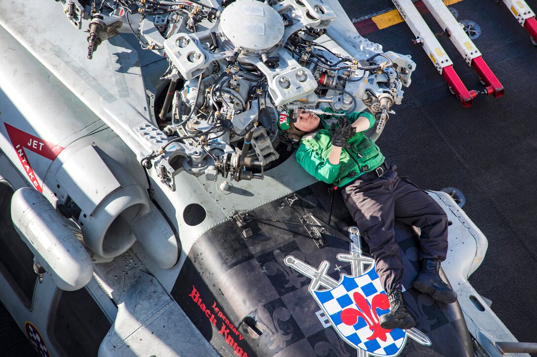 A sailor performs maintenance on a military helicopter.