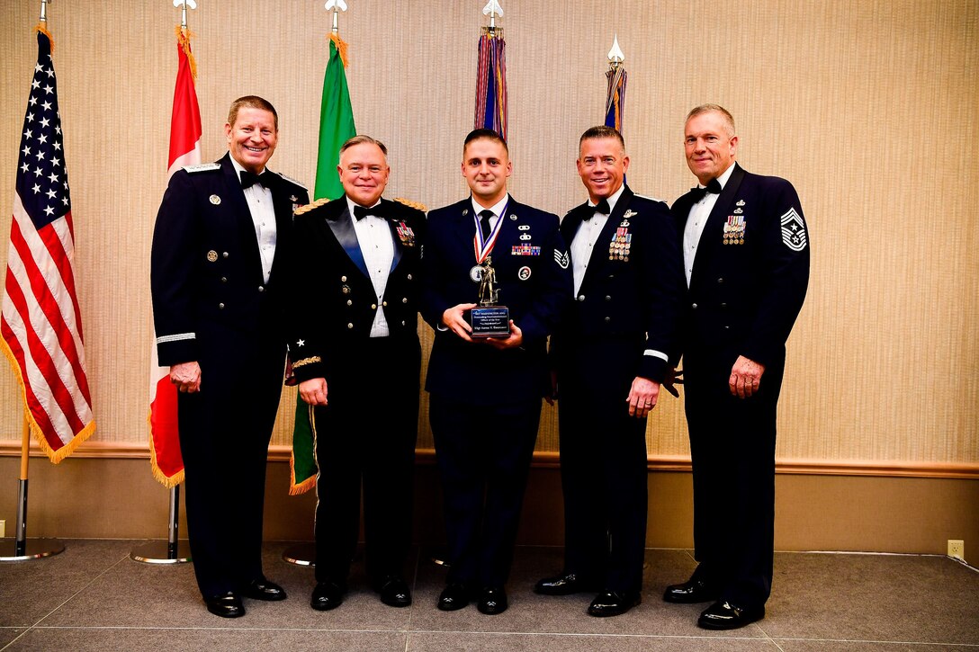 Staff Sgt. Aaron DeCremer, a weapons director with the 225th Air Defense Squadron, Western Air Defense Sector, is presented with the Non-Commissioned Officer of the Year trophy at the Washington Air National Guard’s 9th Annual Awards Banquet held at the American Lake Conference Center on Joint Base Lewis-McChord, Washington, Jan. 27, 2018. DeCremer was awarded the trophy for his outstanding contributions to the Washington Air National Guard over the last year.  Pictured from left to right are: Gen. Robin Rand, Air Force Global Strike Command and Air Forces Strategic-Air, U.S. Strategic Command commander; Maj. Gen. Bret Daugherty, Adjutant General of the Washington National Guard, DeCremer, Brig. Gen. Jeremy Horn, commander of the Washington Air National Guard, and Chief Master Sgt. Max Tidwell, WA ANG command chief. (U.S. Air National Guard photo by Tech. Sgt. Timothy Chacon)