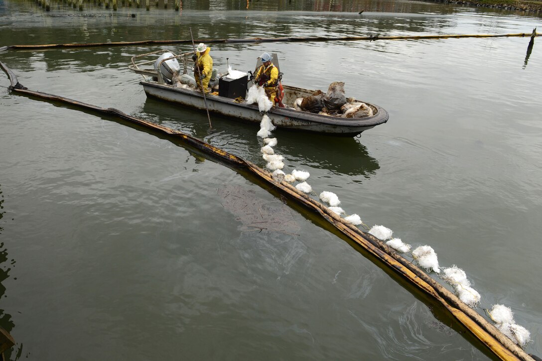 Two oil spill responders in a small boat laying out pompoms.
