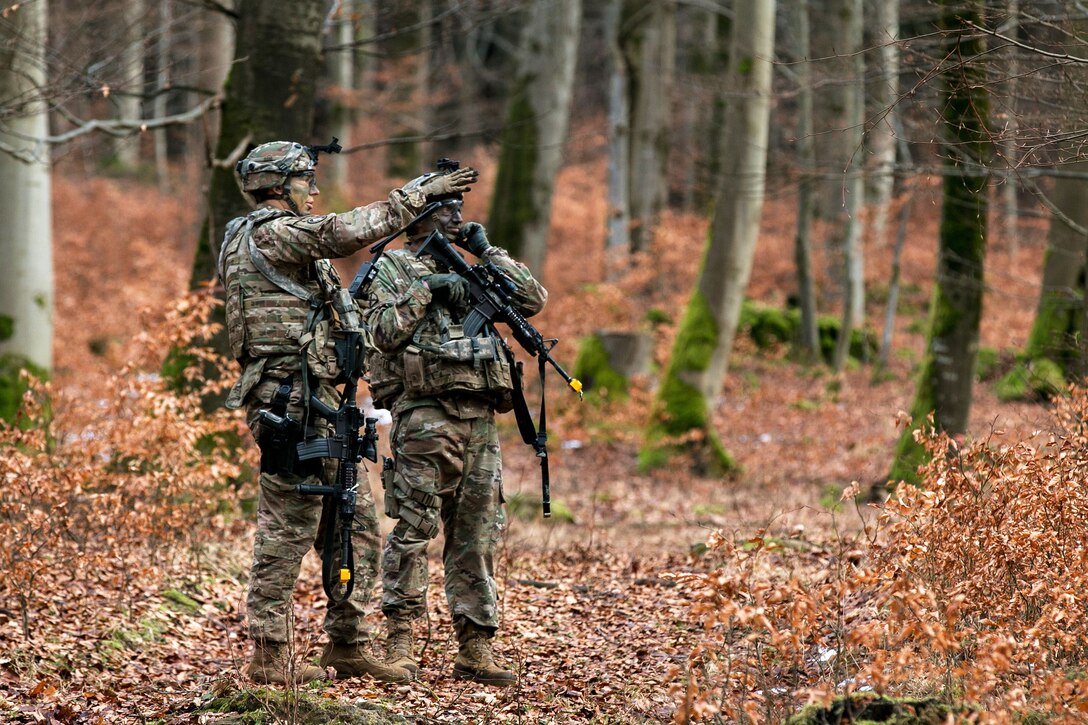 Two soldiers scan the surrounding wooded area.