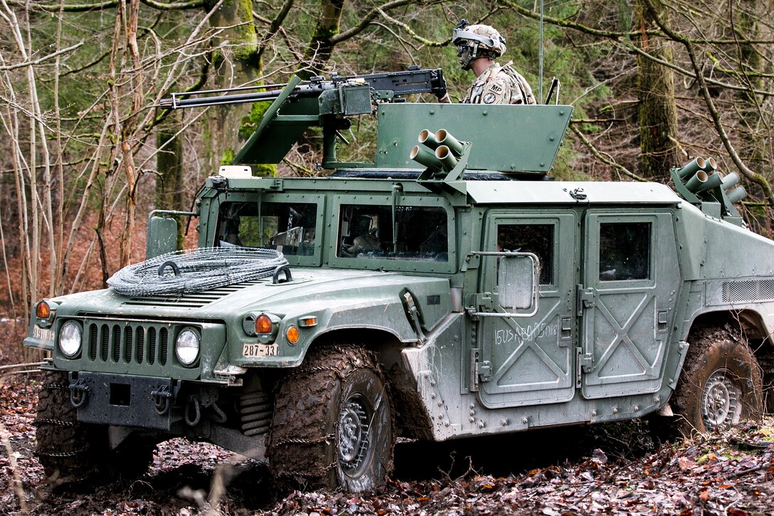 A soldier manning a machine gun on top of a Humvee in a wooded area.