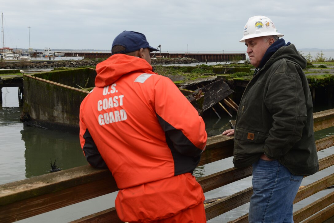 A Coast Guardsman talking with a salvage supervisor on a bridge over a waterway.