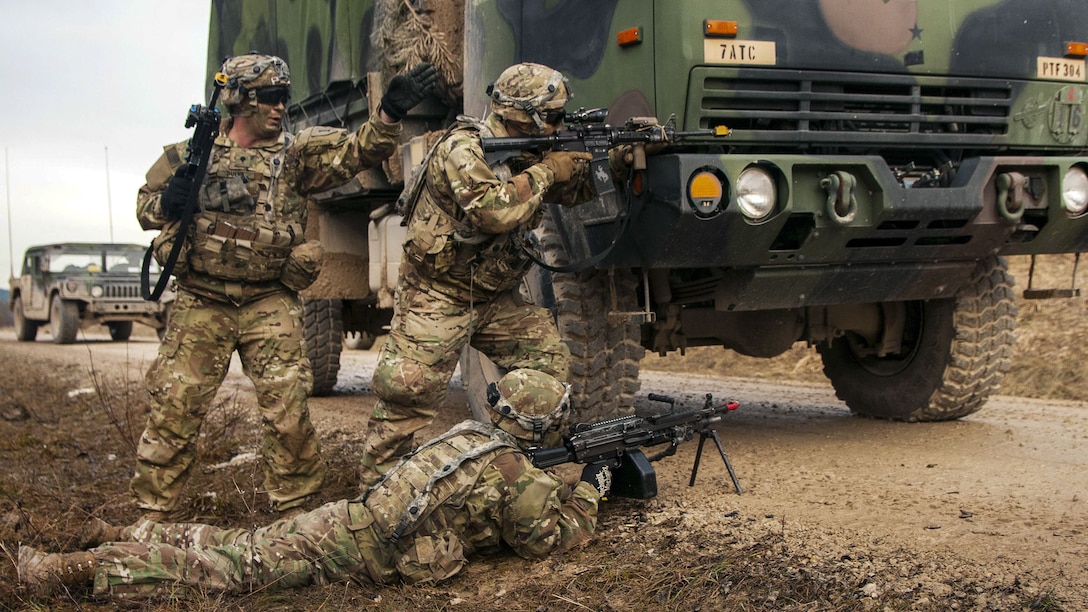 Soldiers fire weapons as they react in front of a vehicle during training.