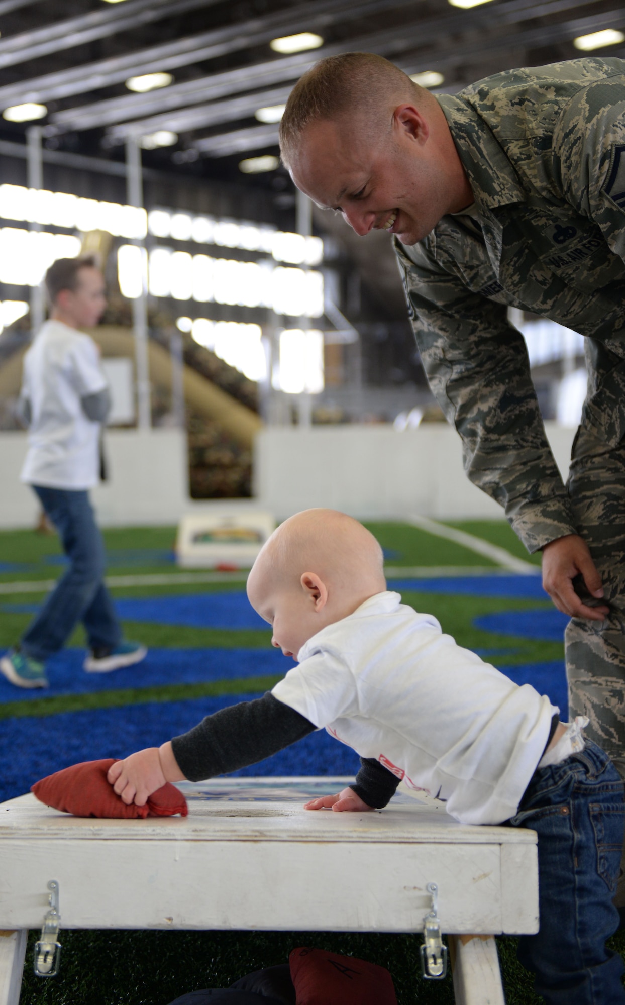 Master Sgt. Michael Cromer, a flight line expeditor assigned to the 28th Aircraft Maintenance Squadron, watches his son, Jonah, play with a bean bag at the Pride Hangar at Ellsworth Air Force Base, S.D., Jan. 29, 2018. B-1 bombers from the 37th Bomb Squadron and Airmen from the 37th Aircraft Maintenance Unit were deployed to Andersen AFB, Guam, to take part in the Continuous Bomber Presence mission. (U.S. Air Force photo by Airman 1st Class Nicolas Z. Erwin)
