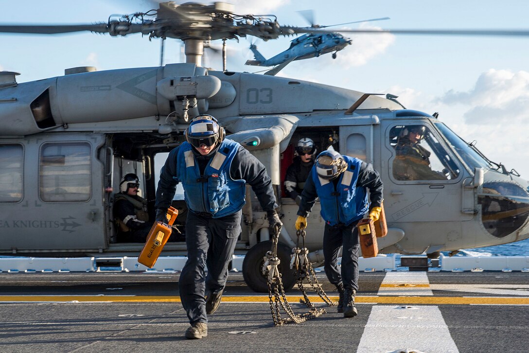 Sailors run from a helicopter after removing its chocks on a flight deck.