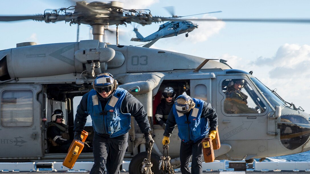 Sailors run from a helicopter after removing its chocks on a flight deck.