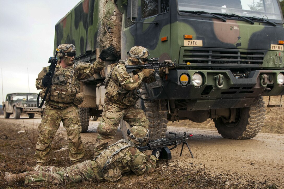 Soldiers fire weapons as they react in front of a vehicle during training.