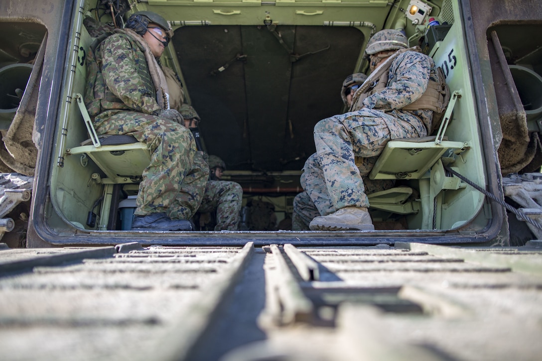 Marines and Japanese soldiers sit in the back of an amphibious assault vehicle.