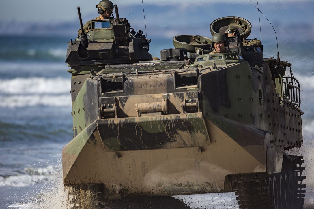 Marines and Japanese soldiers ride in a vehicle along a coastline.