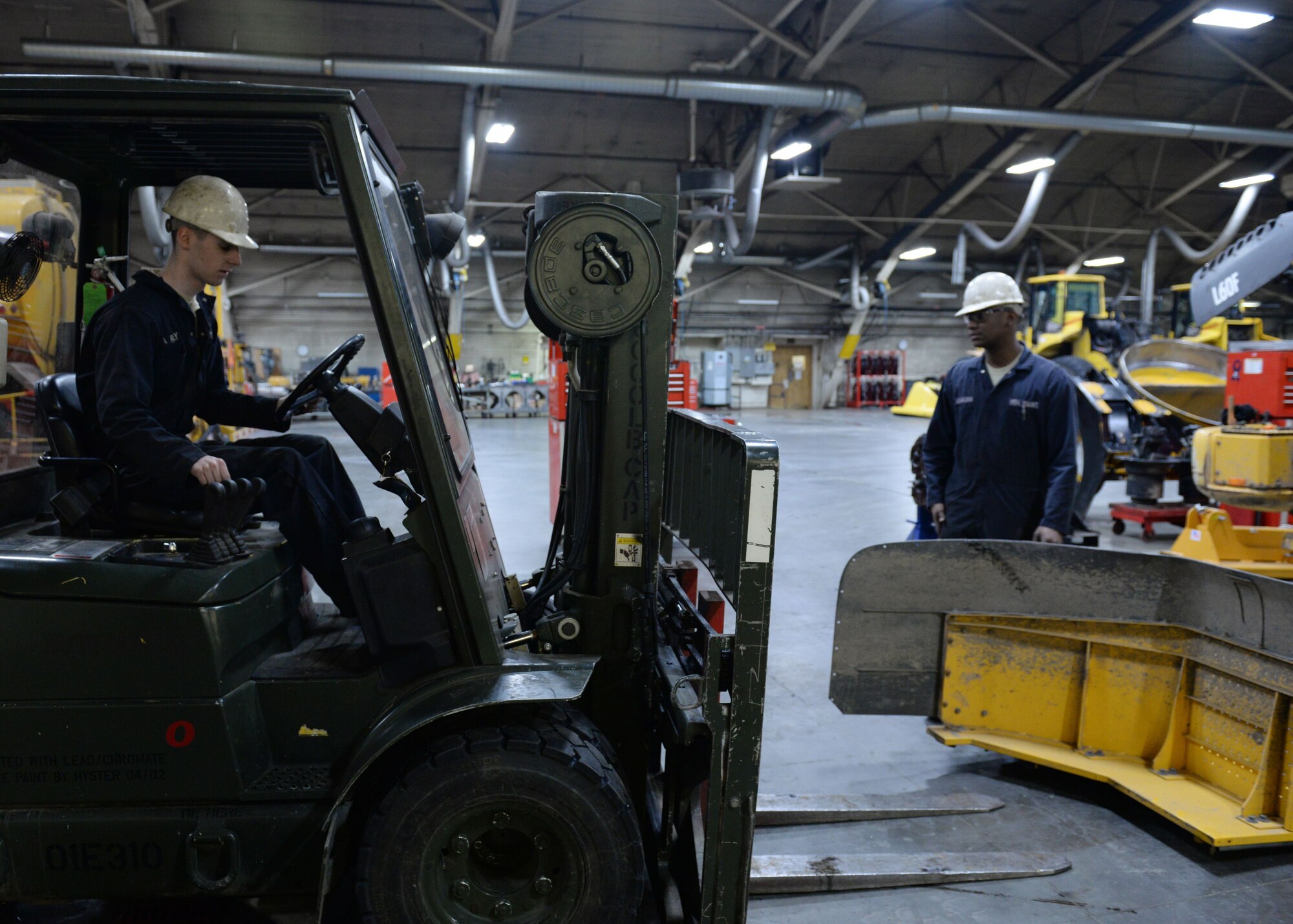 Airman 1st Class Henry Wilson, a mission general vehicle equipment maintenance apprentice, with the 673d Logistics Readiness Squadron Vehicle Maintenance, Heavy Equipment shop, watches for safety as Senior Airman Samuel Reilly, a mission general vehicle equipment maintenance journeyman with the 673d Logistics Readiness Squadron Vehicle Maintenance, Heavy Equipment shop uses a forklift to pick up a side panel for a L60F loader, Jan. 25, 2018, at Joint Base Elmendorf-Richardson, Alaska. The Heavy Equipment shop repairs and services all snow-removal and road equipment at JBER.