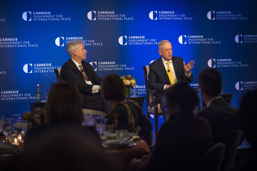 Defense Secretary James N. Mattis talking to an audience while seated on stage with an ambassador.