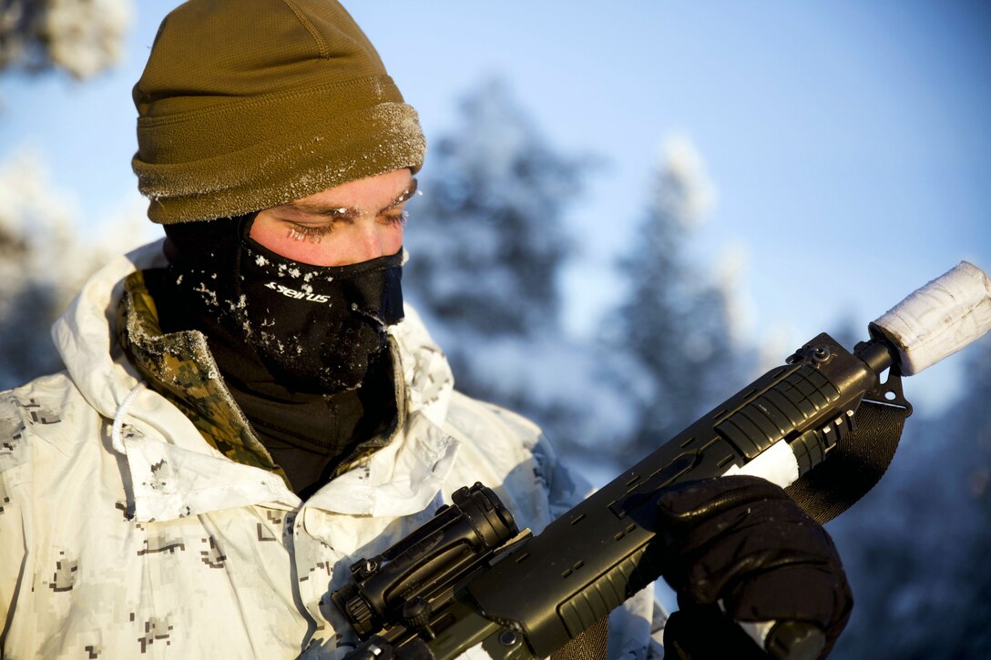 A Marine in heavy winter clothing inspects his rifle.