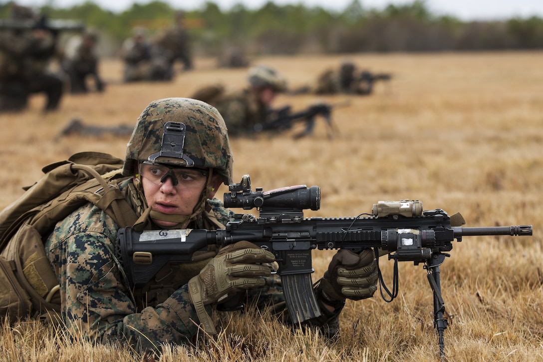 A Marine holds a gun in a field during training exercise.