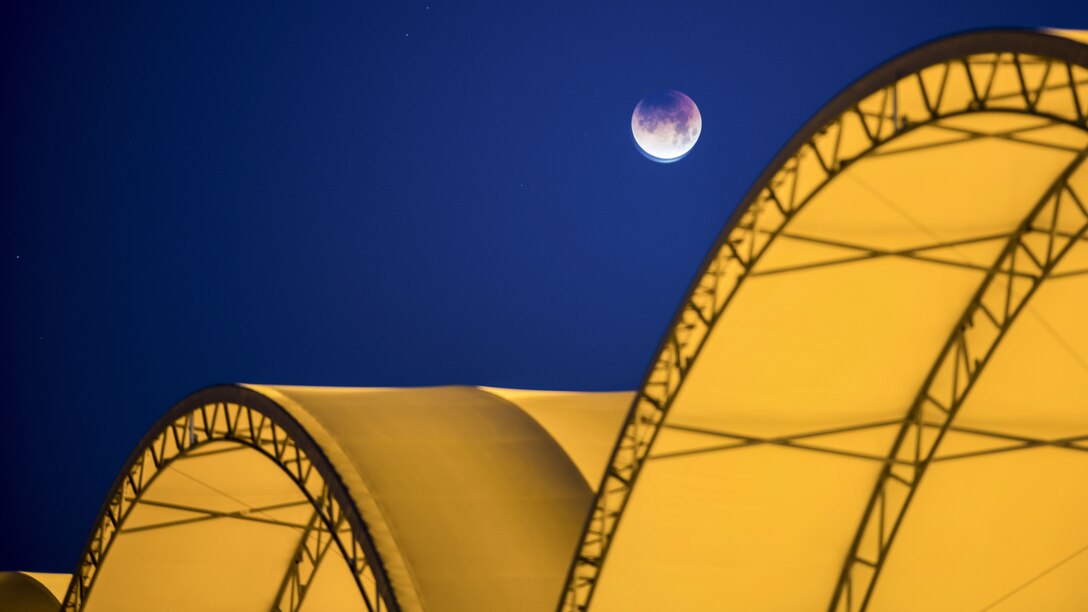 A moon sets against a midnight blue sky over yellow hangar canopies.