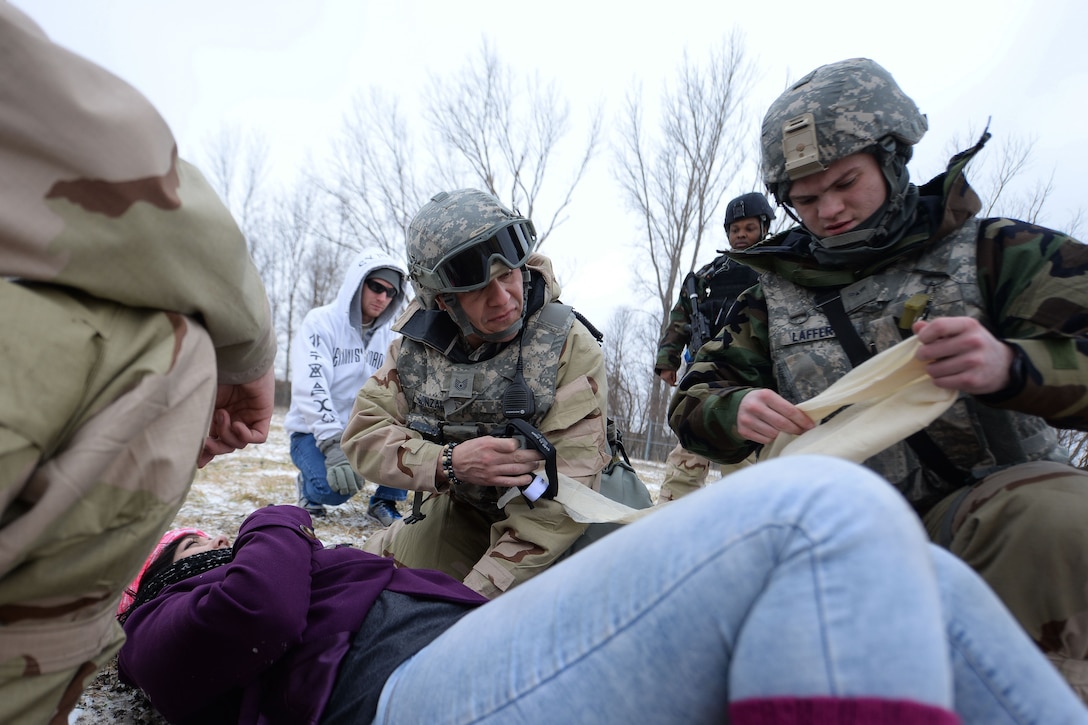 Two airmen hold bandages for a person laying on the ground.