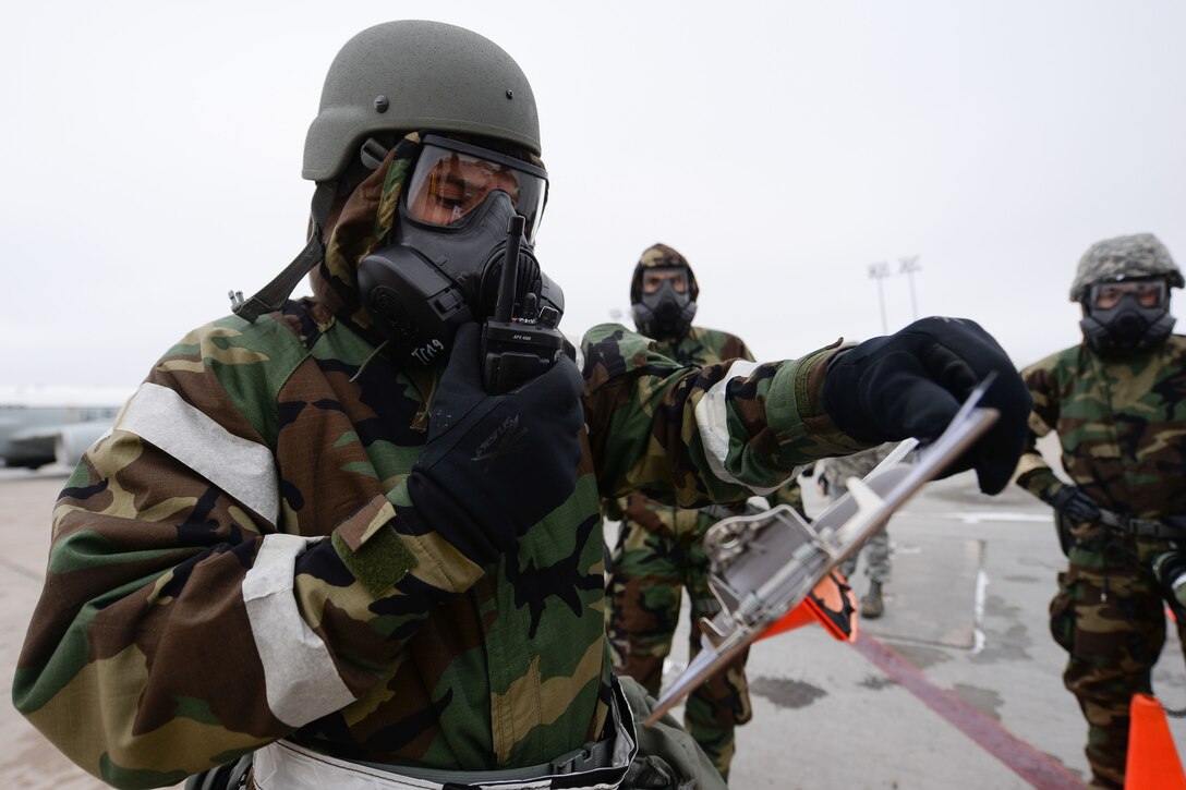 Three airmen wear gas masks on a runway.