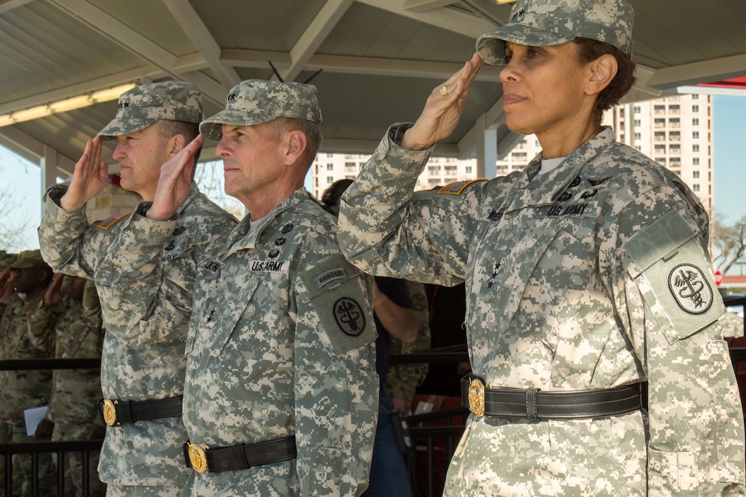 An army Lt. Gen. salutes with two other people during a ceremony.