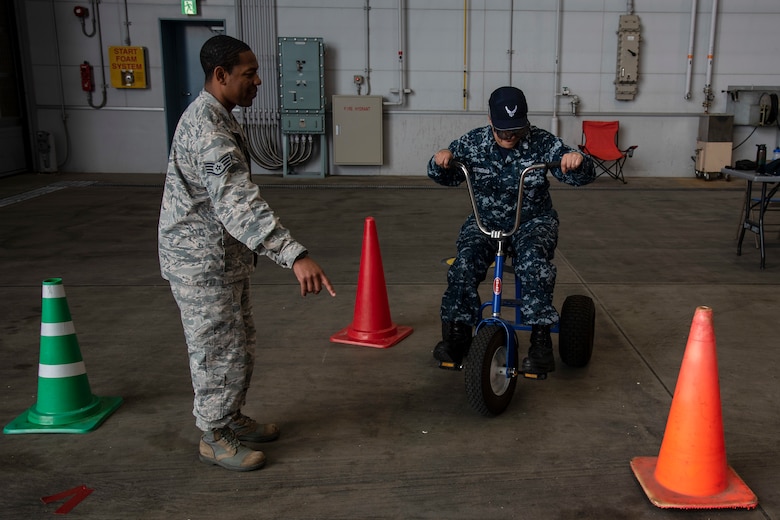 U.S. Air Force Staff Sgt. Dorian Lewis, a 35th Fighter Wing occupational safety technician, instructs Petty Officer 1st Class Aurora Contreras, a Naval Air Facility Misawa aviation maintenance administrator, while riding a bike wearing Fatal Vision goggles during the 75th Safety Convention at Misawa Air Base, Japan, May 24, 2018. This demonstration educated participants on how alcohol misuse can create dangerous situation while operating a motor vehicle. (U.S. Air Force photo by Airman 1st Class Collette Brooks)