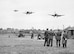 Personnel of No.121 (Eagle) Squadron look on as three Supermarine Spitfire aircraft land after a fighter sweep over northern France at Royal Air Force Rochford in Essex, England August 1942. Some of the accommodation used by the squadron is visible in the background, as are several civilian houses and two RAF vehicles. (Courtesy photo)