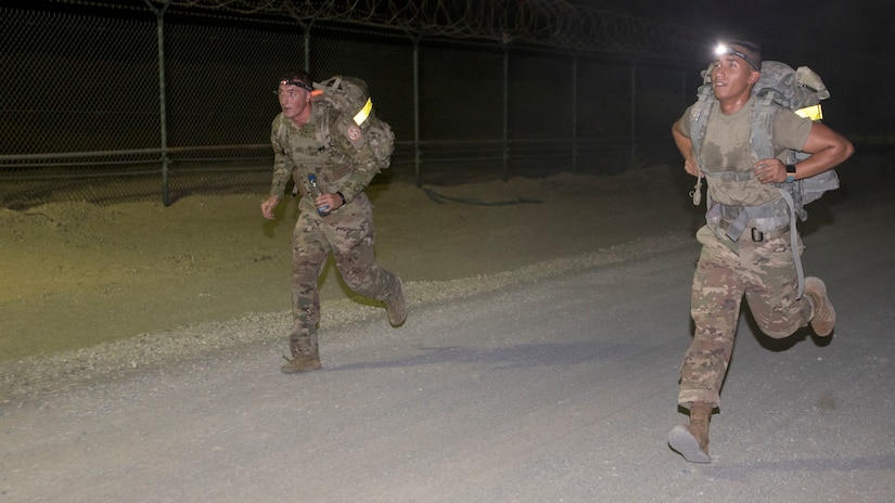 U.S. Army Spc. Austin Mellon, left, a cavalry scout assigned to Charlie Troop, 1st of the 124th Cavalry, U.S. Army Central, and U.S. Army Spc. Joselito Reyes, a wheeled vehicle mechanic assigned to Charlie Battery, 5th of the 52nd Air Defense Artillery Battalion, USARCENT, fight for a lead over each other during the ruck march at USARCENT's Best Warrior Competition at Camp Arifjan, Kuwait, June 28, 2018. Ruck marches provide Soldiers with an opportunity to test themselves against their peers and strengthen cohesion between competing units.