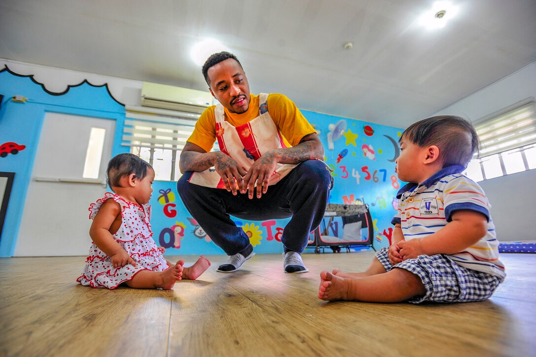 A sailor plays with two toddlers on the ground.